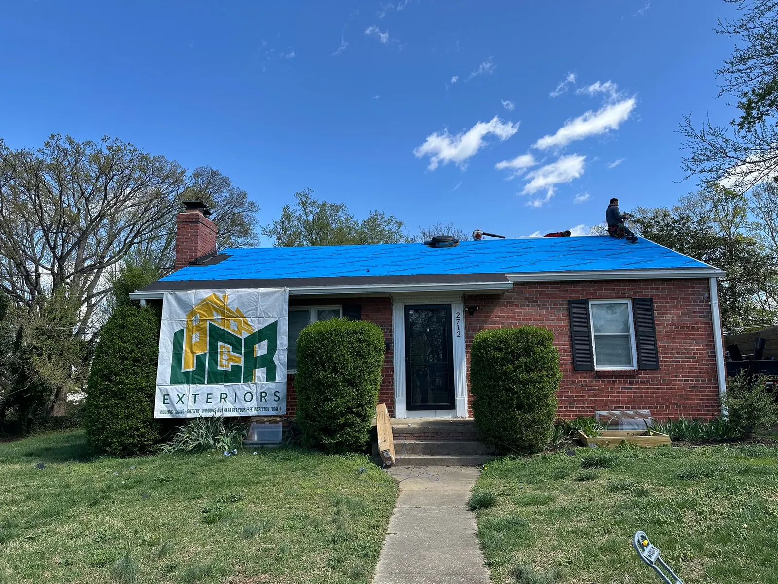 Brick Northern Virginia home with its roof tarped by LCR after storm damage, LCR Exteriors sign in the front yard