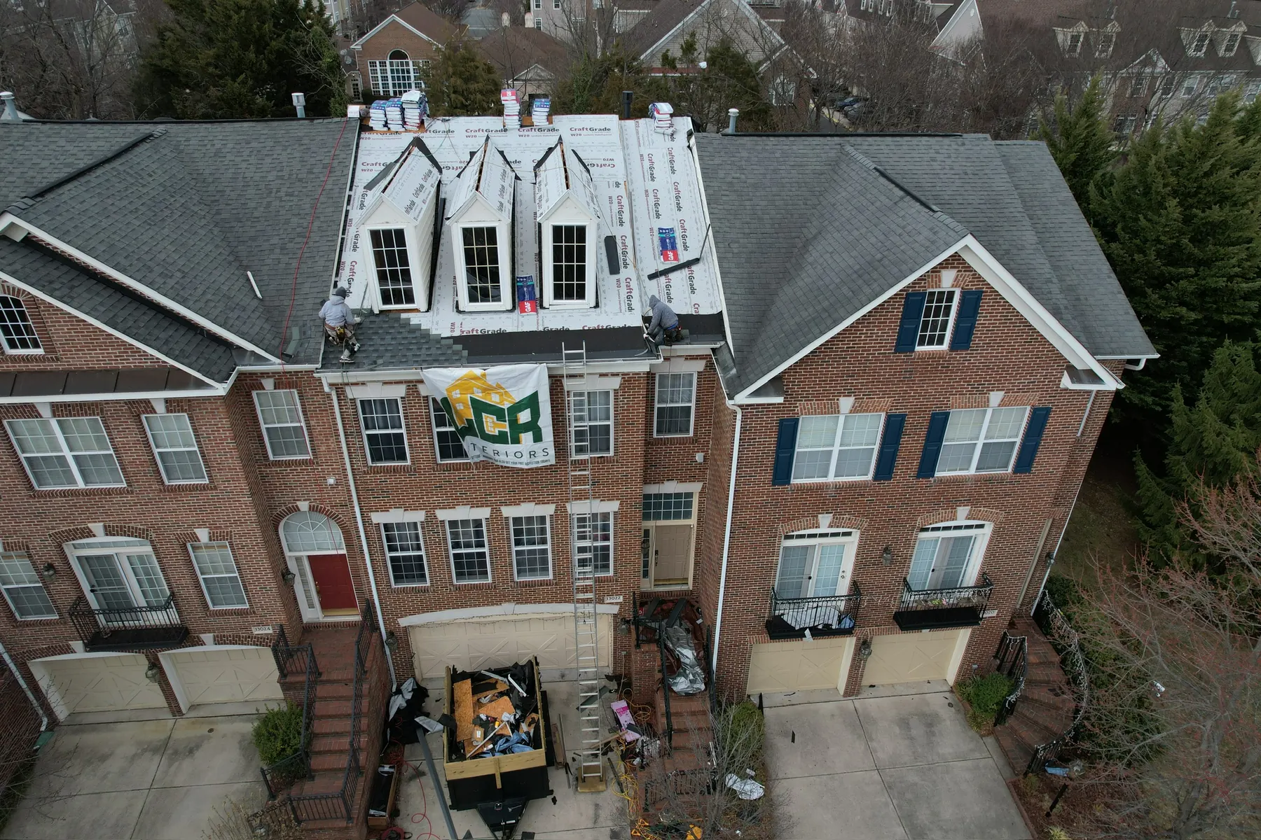 Drone view of an LCR crew re-roofing a brick townhouse row, LCR Exteriors banner on the front