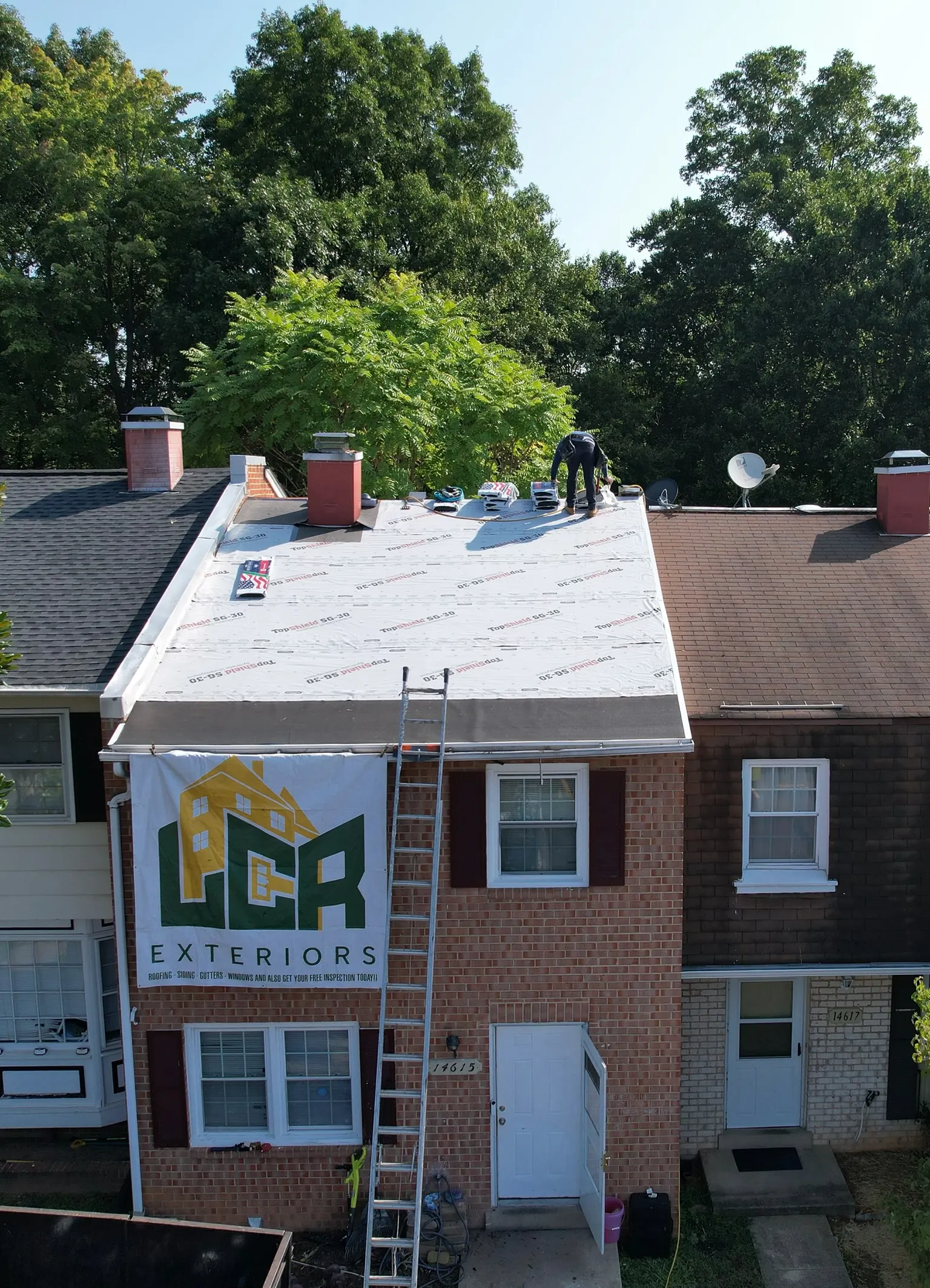 Aerial of an LCR roof replacement in progress: underlayment down, crew at the ridge, LCR Exteriors banner on the house